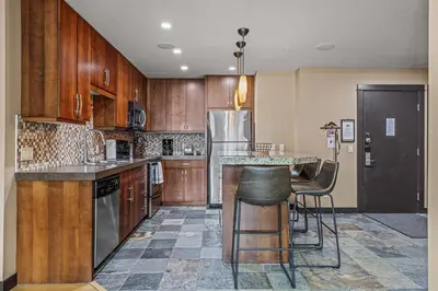 a kitchen with wooden cabinets and a table with bar stools at Stunning Condo - Hot Tubs & Steam Room - Pets Ok in Canmore
