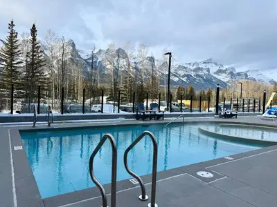 a large swimming pool with mountains in the background at Brand New Canmore Studio - Cozy Mountain Getaway in Canmore