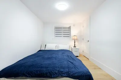 a white bedroom with a blue bed and a lamp at Bright & Modern Surrey Basement Suite with Queen Beds & Parking in Surrey