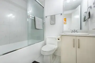 a white bathroom with a toilet and a glass shower at Bright & Modern Surrey Basement Suite with Queen Beds & Parking in Surrey