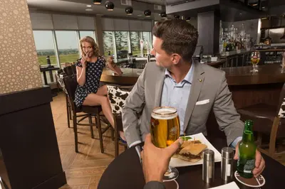 a man and woman sitting at a table with a glass of beer at Applause Hotel Calgary Airport by CLIQUE in Calgary