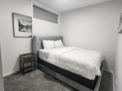 a white bedroom with a bed and a night stand at Stylish furnished 2bedroom suite near YYC Airport in Calgary