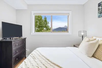 a white bedroom with a bed and a window at Newly Renovated 3BR Condo with Hot Tub and MTN Views in Canmore