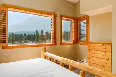 a bedroom with a bed and a large window at Spectacular 3BR Mountain Views with Hot Tub and Gym in Canmore
