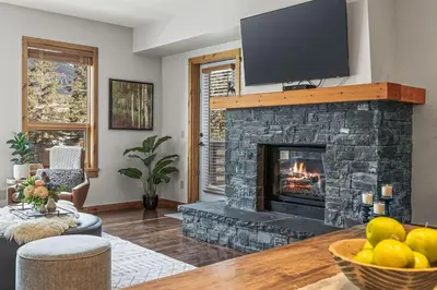 a living room with a stone fireplace with a flat screen tv at 2BR Modern Luxe Condo with Hot Tub and Views in Canmore