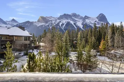 a house with a snow covered mountain in the background at Mountain Views Lux 2BR Condo in Canmore with Hot Tub in Canmore