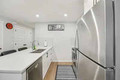 a white kitchen with a stainless steel refrigerator at Deluxe 2-Bedroom Getaway Near Mahogany Lake in Calgary