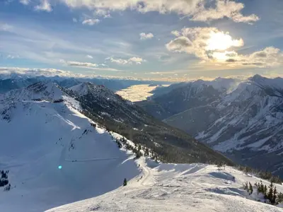 a view of a snowy mountain with the sun in the background at Mountaineer Creekside Cabin - Private Hot Tub in Golden