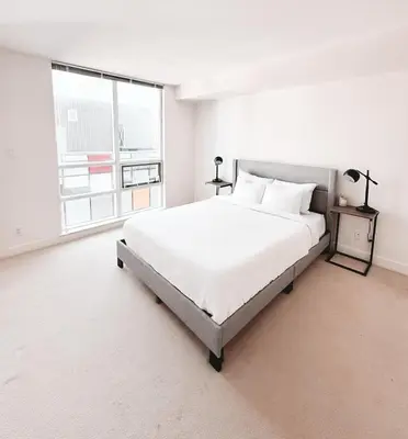 a white bedroom with a bed and a large window at Riverside Mint 2bd den 2 ba in Calgary