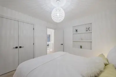 a white bedroom with a large bed and a chandelier at Board Games, King Bed, Cocoa Bar, & Firewood! in Calgary