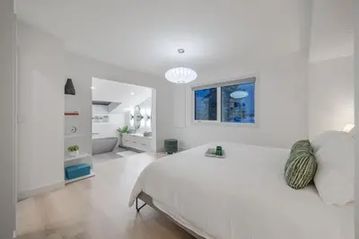 a white bedroom with a large bed and a bathroom at Board Games, King Bed, Cocoa Bar, & Firewood! in Calgary