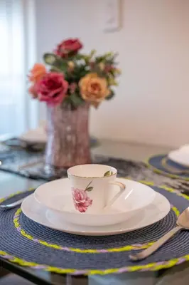 a cup and plates on a table with a vase of flowers at New Quiet Charming 1BR Suite near UBC & PW Park in Vancouver