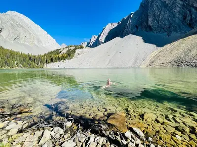 a person swimming in a lake in the mountains at Luxury 2 Bedroom Mountain View Condo in Canmore