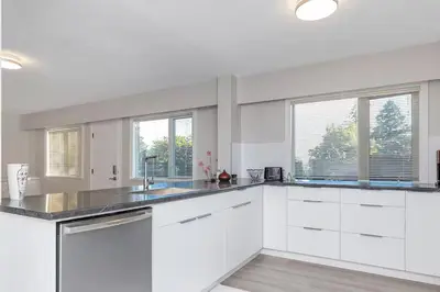 a white kitchen with white cabinets and windows at Spacious Oceanview Suite with Private Entrance in West Vancouver