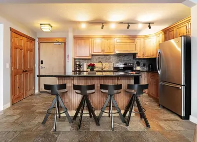 a kitchen with wooden cabinets and black bar stools at Rocky Mountain Retreat-Mountain View! in Canmore