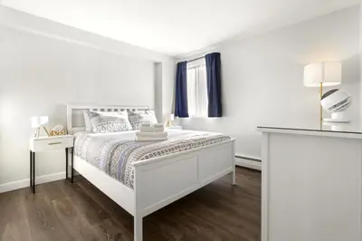 a white bedroom with a bed and a window at Chic & Spacious 2BR at Stampede with Parking, AC in Calgary