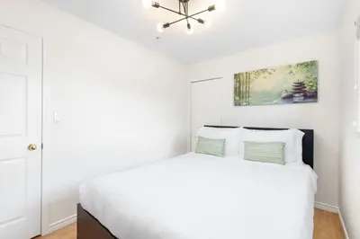 a white bedroom with a white bed and a chandelier at NEW Roomy 3BR Family Suite. 5 min to Skytrain. in Vancouver