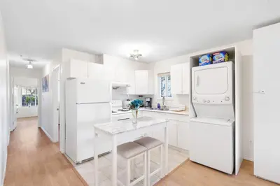 a white kitchen with a white refrigerator and a table at NEW Roomy 3BR Family Suite. 5 min to Skytrain. in Vancouver