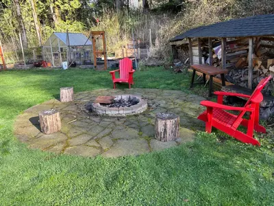 a fire pit in a yard with two red chairs and logs at Sumas Mountain basement suite in Abbotsford