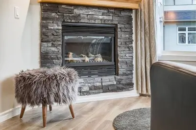 a living room with a stone fireplace with a chair at Charming 2BR Condo with Spectacular Mountain Views in Canmore
