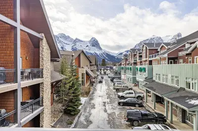 a snowy street in a town with mountains in the background at Splendid Mountain View 2BR Condo with Pool and Hot Tub in Canmore