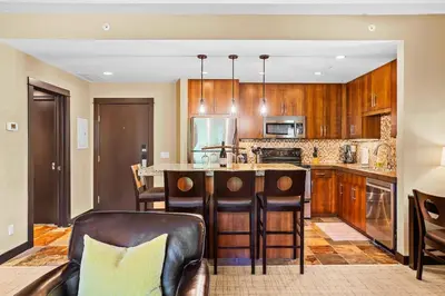 a kitchen with wooden cabinets and an island with chairs at Ideal 2BR Canmore Haven Hot Tub plus Stunning Views in Canmore
