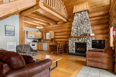 a living room with a stone fireplace in a log cabin at Beautiful Rustic Chalet in the Heart of Rockies in Golden