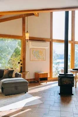 a living room with a wood stove in a room with windows at First Light - Vintage waterfront with hot tub - One Bedroom in Tofino