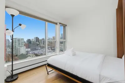 a bedroom with a white bed and a large window at Downtown Skyline Suite with Pool & Sauna in Vancouver