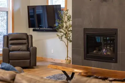 a living room with a fireplace and a chair and a tv at Moose Lodge by Fernie Central Reservations in Fernie