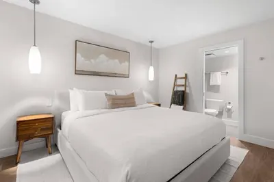 a white bedroom with a white bed and a bathroom at 2BR + Sofabed | Gables | Epic Village Location | Secure Parking | Stylish & Cozy in Whistler