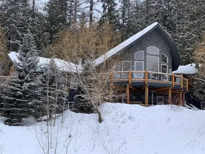a house in the woods with snow on the ground at Snowed Inn Chalet by Fernie Central Reservations Right on the Slopes in Fernie