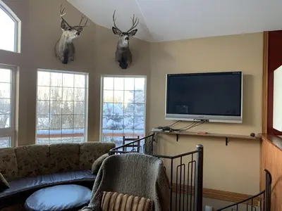 a living room with a tv and deer heads on the wall at Snowed Inn Chalet by Fernie Central Reservations Right on the Slopes in Fernie