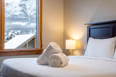 a bedroom with two beds and a window with snow covered mountains at Alpine Chic - two-story mtn escape near downtown in Canmore