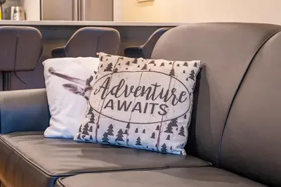 a pillow that says adventure awaits sitting on a couch at Alpine Chic - two-story mtn escape near downtown in Canmore