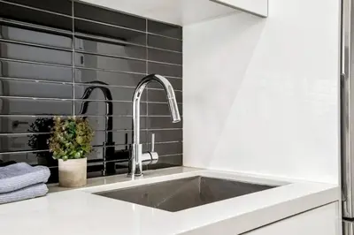 a kitchen with a sink and a black tile wall at Modern 1BR City Escape with Balcony near DT Calgary in Calgary
