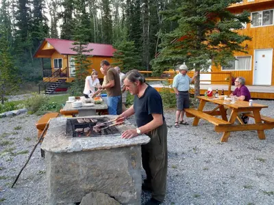 a group of people standing around a stone grill at Northern Rockies Lodge in Muncho Lake
