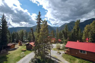 a cabin with a red roof and mountains in the background at Northern Rockies Lodge in Muncho Lake