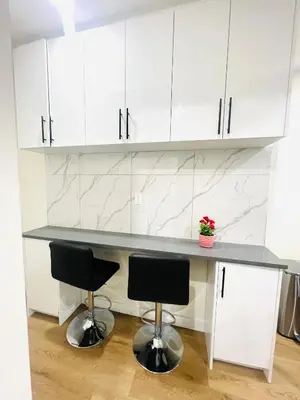 a kitchen with white cabinets and a counter with two stools at West Edmonton- Rose in Edmonton