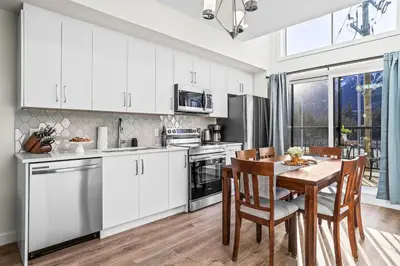 a kitchen with white cabinets and a wooden table at 3BR Rockies Haven Near Banff with Private Patio in Canmore