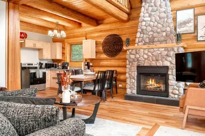 a living room with a stone fireplace in a log house at Rustic Cabin Hideaway with BBQ Fire Pit and Mtn Views in Golden