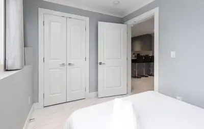 a white bedroom with two doors and a bed at Large 3 Bedroom Laneway House in Vancouver