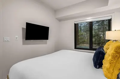 a white bedroom with a bed and a flat screen tv at King Beds Fire Place New Build in Canmore