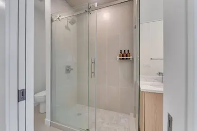 a shower with a glass door in a bathroom at Shaganappi 2BR with private Baths, Walk to CTrain, Garage Parking, Full Kitchen in Calgary
