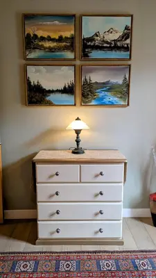 a dresser with a lamp on top of it with three paintings at 2 Bedroom Condo Banff, Canmore sleeps 6 comfortably in Canmore
