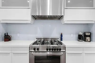 a kitchen with a stainless steel stove and white cabinets at Calgary Mini Manor Near DT Sleeps 8 Prime Location in Calgary