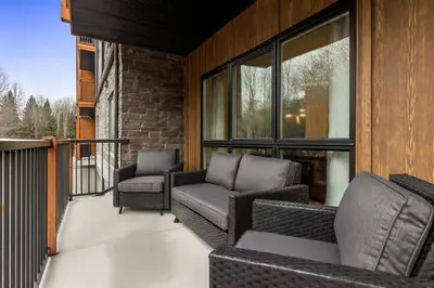 a patio with two chairs and a couch on a balcony at Brand New 3BR Rockies Haven w/ Balcony, Pool & Gym in Dead Man's Flats