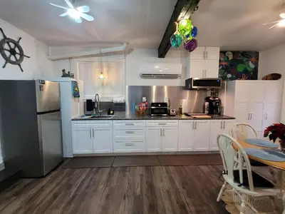 a kitchen with white cabinets and a refrigerator and a table at Nesting Ravens cottage in Nanaimo