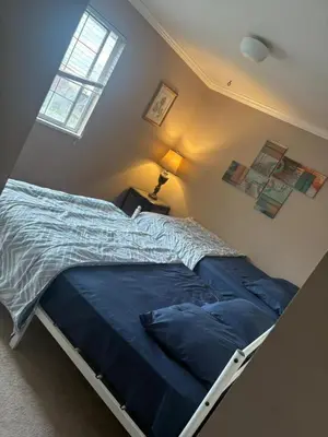 a bedroom with a bed with a blue comforter and a window at Surrey- Delta Budget Guest House - Private Rooms & Suites, Free Parking & Fast Wi-Fi in Surrey
