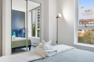 a white bedroom with a mirror and a bed at Stylish 2BR Downtown Condo By Arena Free Parking in Vancouver